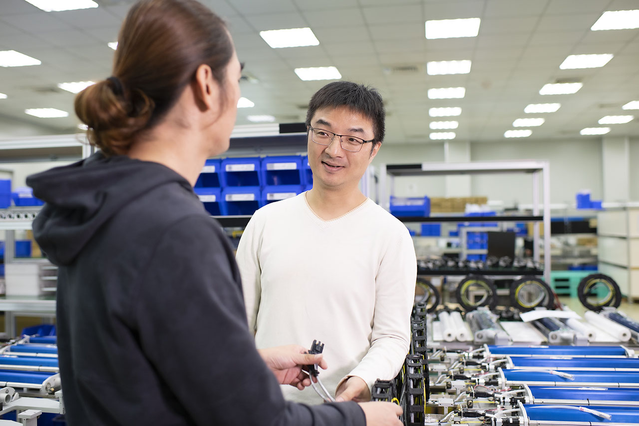 瑞健科技資深工程師 Weber Yu 和同仁，背景為 PCB 印刷電路板設備零件模組生產線。